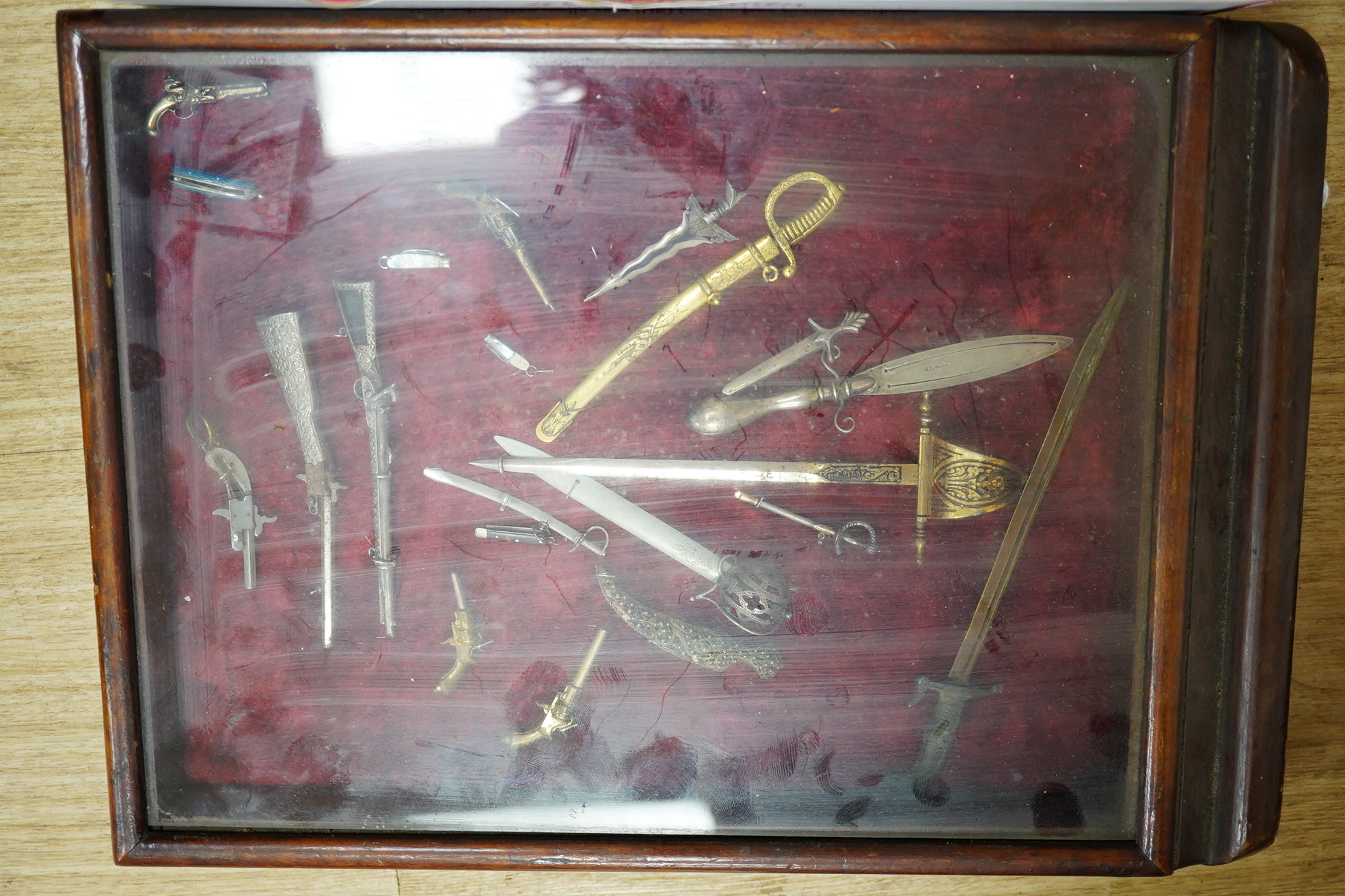 A large collection of miniature weapons, comprising approximately thirty-four edged weapons, and thirteen assorted firearms, approximately half contained within a mahogany case. Condition - fair to good